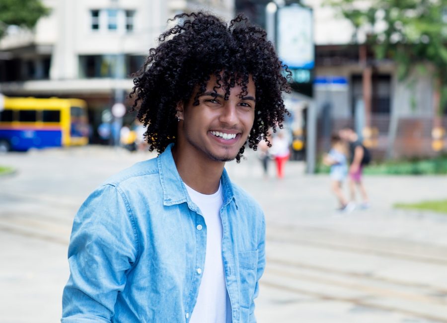 Mexican young adult man with long curly hair outdoor in city in summer